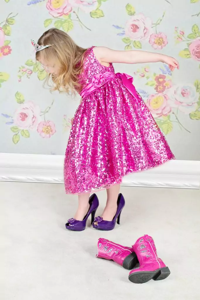 a young girls is trying up high heels in a pink dress